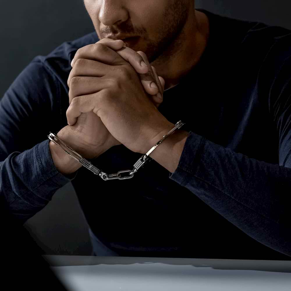 Man wearing handcuffs with hands folded under chin