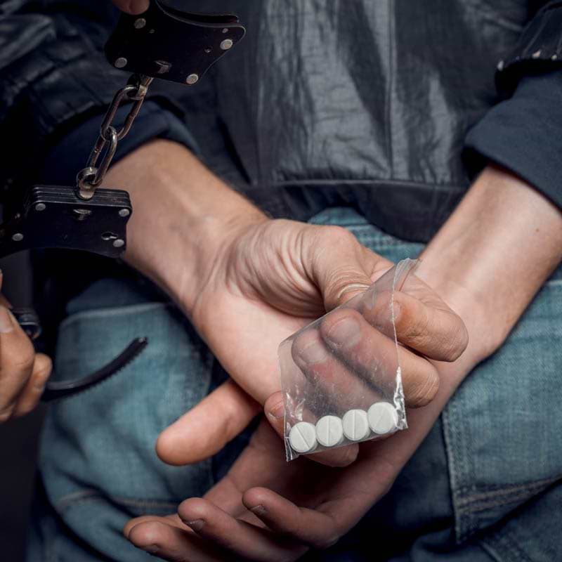 Hands behind back with plastic bag of pills